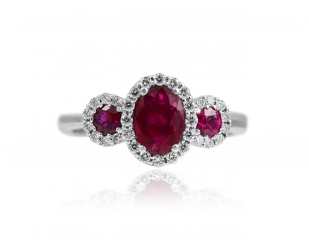 A white gold ring with an oval ruby in the center with halo diamond, and two round ruby with halo on either side